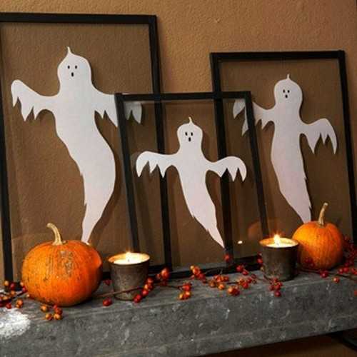 fantome din hartie intr-o rama langa lumanari de Halloween