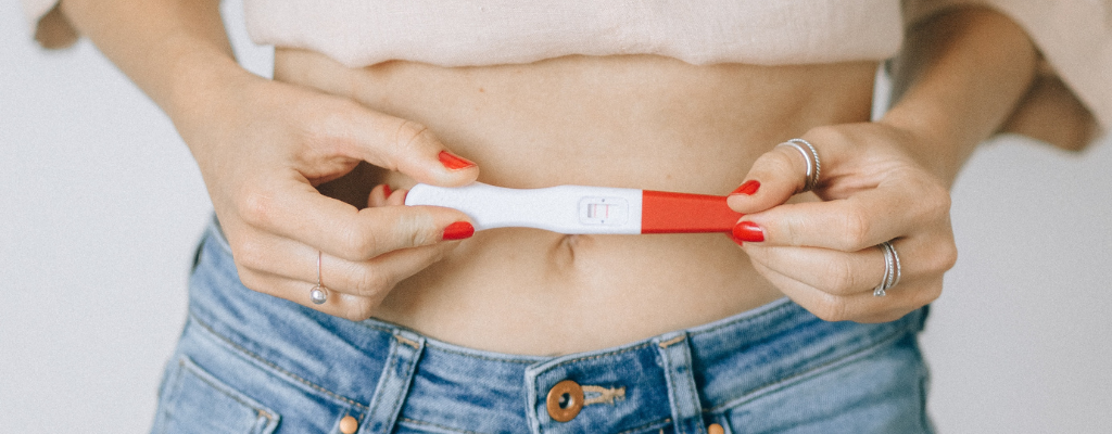 femeie care tine un test de sarcina la nivelul buricului