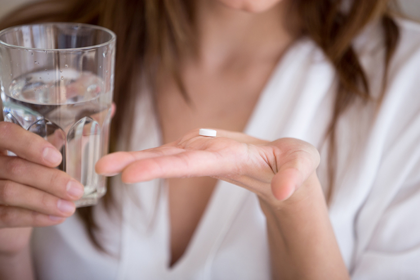 femeie care tine o pastila intr-o mana si in alta un pahar cu apa