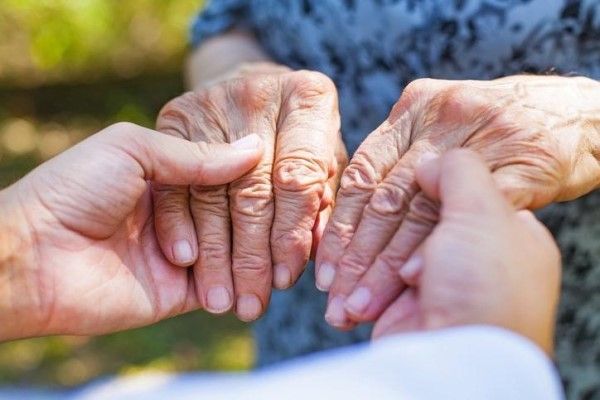 o persoana tanara tine cu propriile maini, mainile ce tremura ale unei batrane