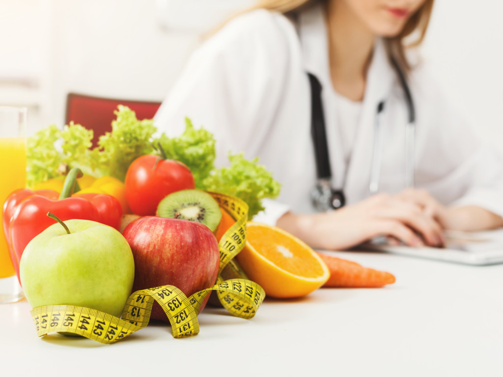 mai multe fructe si legume pe o masa langa un medic