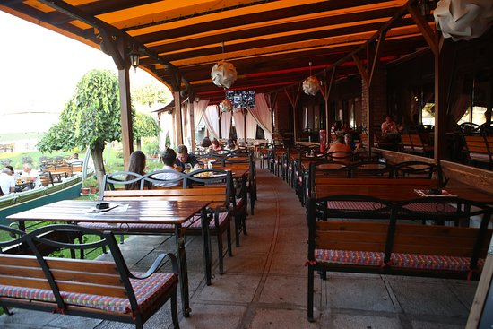 o terasa cu mese si banci din lemn, la care sunt asezate cateva persoane pe timp de zi
