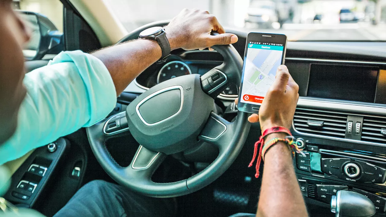  O persoana la volanul unei masini cu un telefon in mana, pe ecranul caruia apare o harta