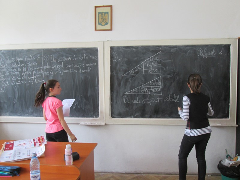 doua eleve care rezolva un exercitiu matematic la tabla cu creta