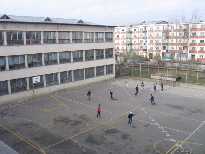 un teren de fotbal si volei in curtea scolii si cativa elevi care e joaca