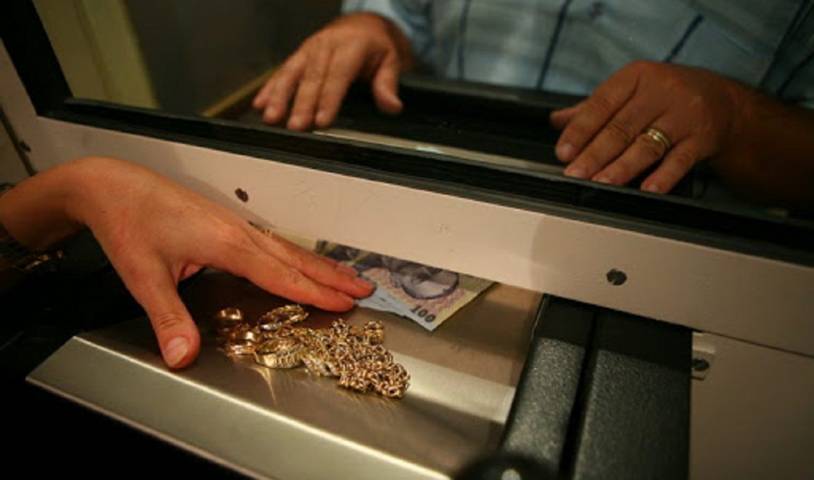 mainile a doua persoane ce fac o tranzactie cu bijuterii din aur contra mai multor bancnote de 100 de lei