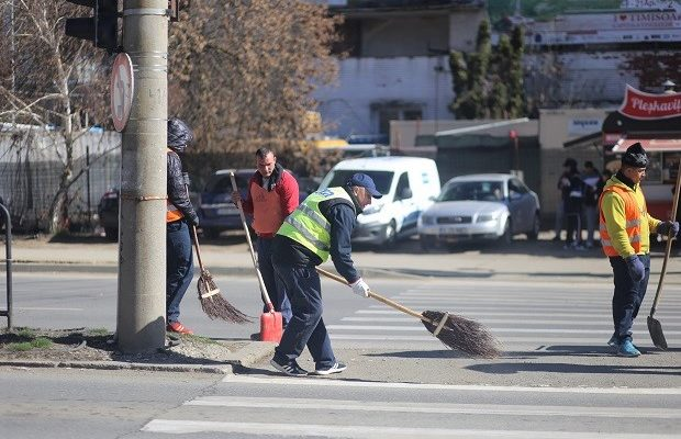 Mai multi barbati care poarta veste reflectorizante curata o portiune de carosabil