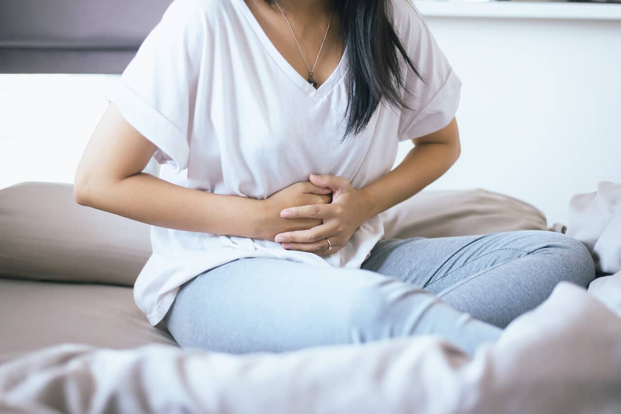 femeie care sta asezata pe pat si se tine de abdomen din cauza durerilor provocate de pancreas