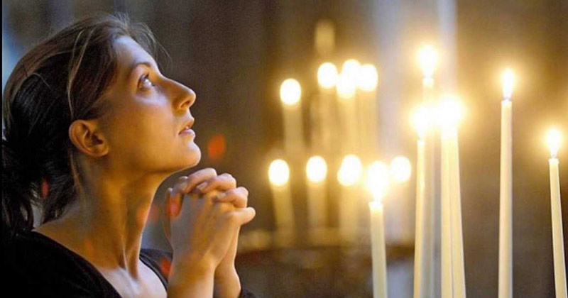 o femeie care se roagă și mai multe lumânări aprinse