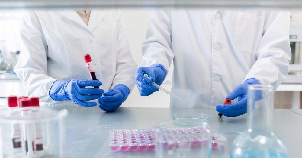 medici care analizeaza o proba de sange intr-un laborator
