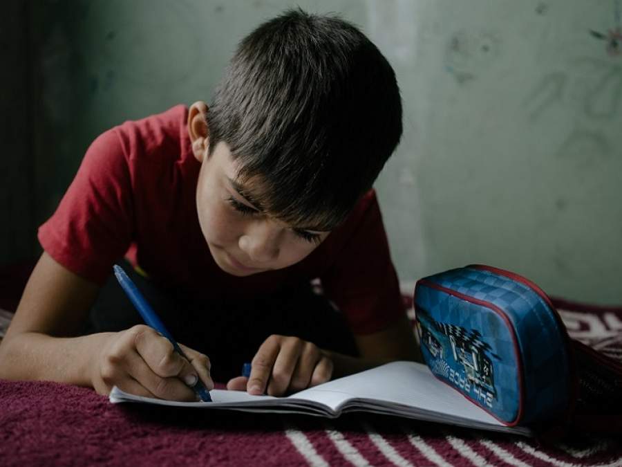 copil care scrie cu un fix pe un caiet si langa el are un penar