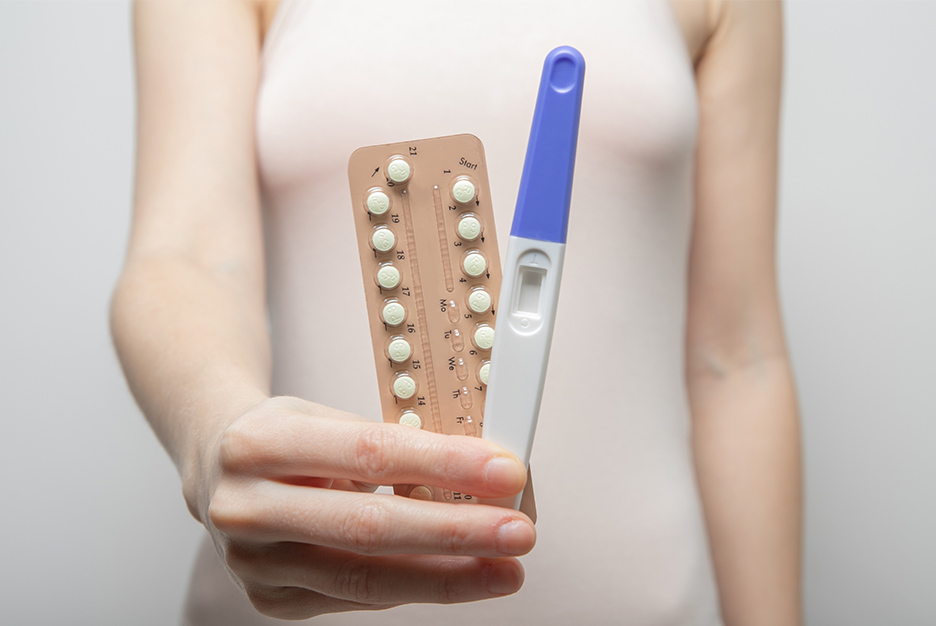 femeie care tine in mana un test pentru sarcina si pastile contraceptive