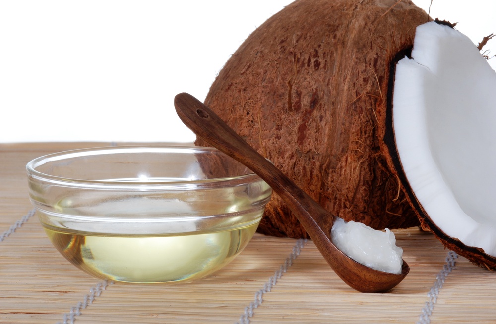 un recipient cu ulei de cocos langa mai multe nuci de cocos pe o masa