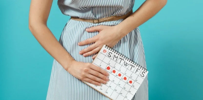 femeie care tine un calendar in mana si se tine de burta