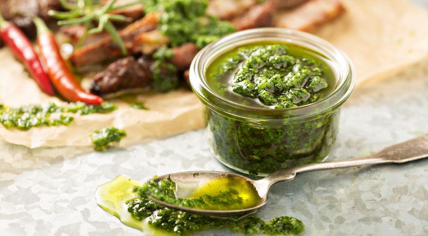 o lingura cu sos chimichurri langa un bol cu sos si carne pe o masa